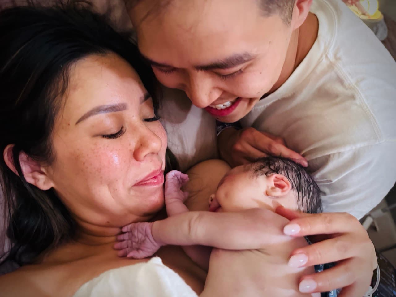 New parents smiling down at their newborn resting skin-to-skin on mom's chest