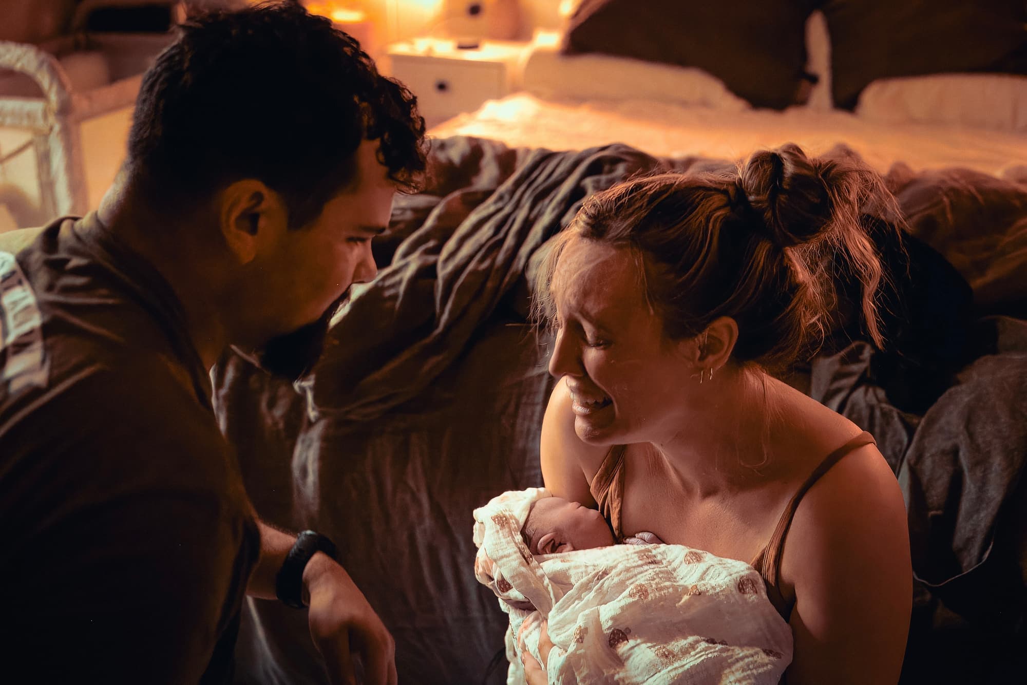 Candlelit home birth with parents forehead-to-forehead holding their swaddled newborn